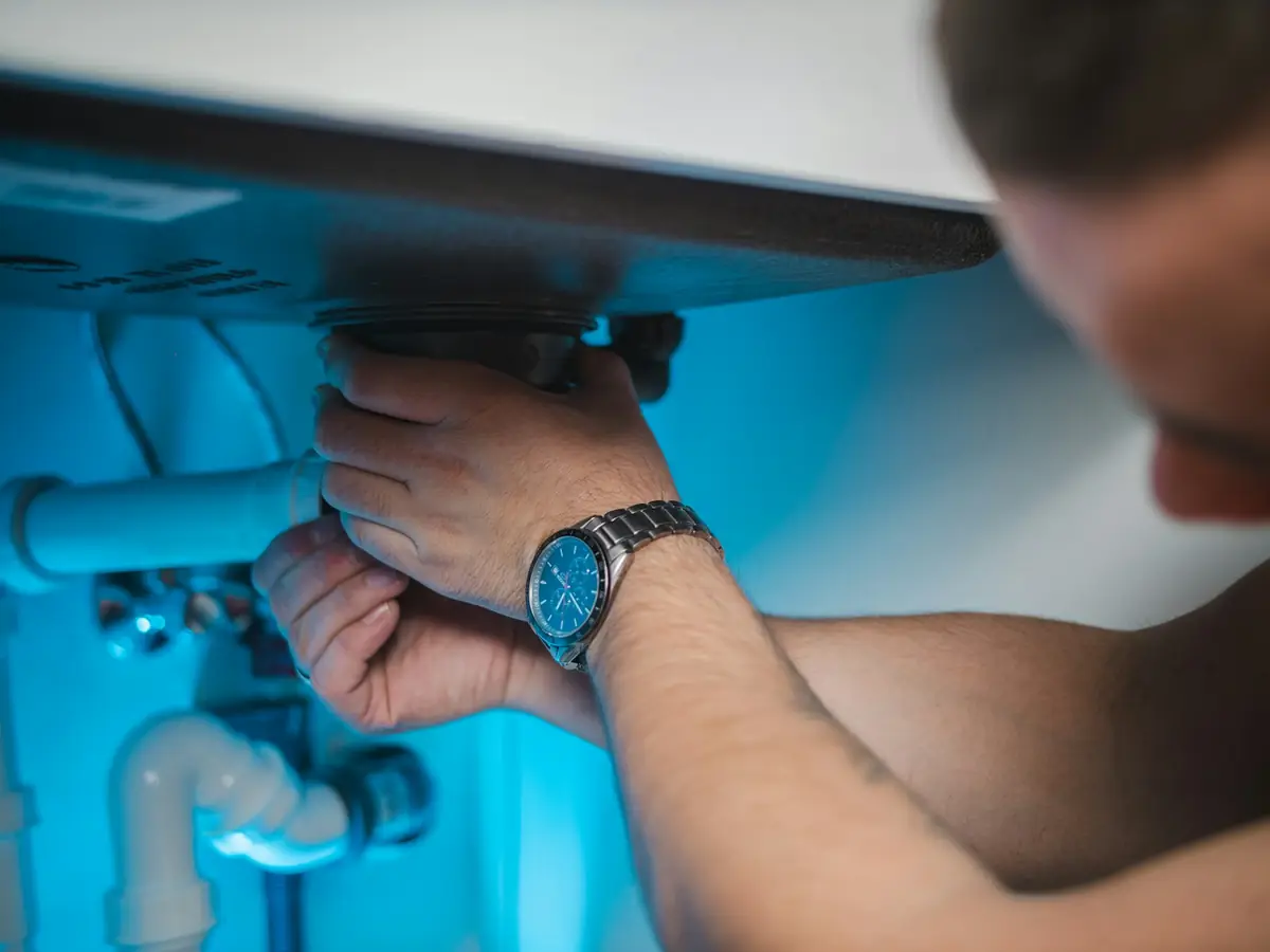 Hands checking the drain connections under a sink for leaks