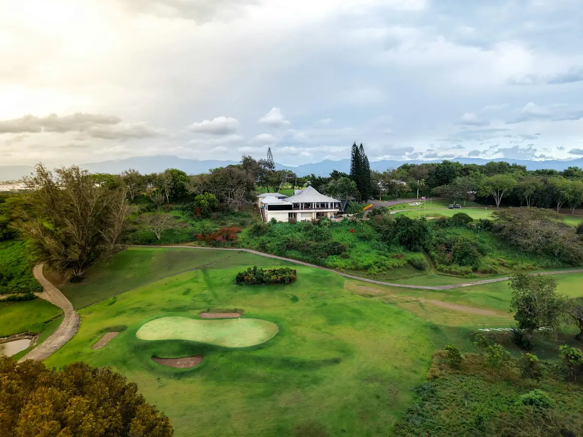 A golf course green with a house on the hill behind it
