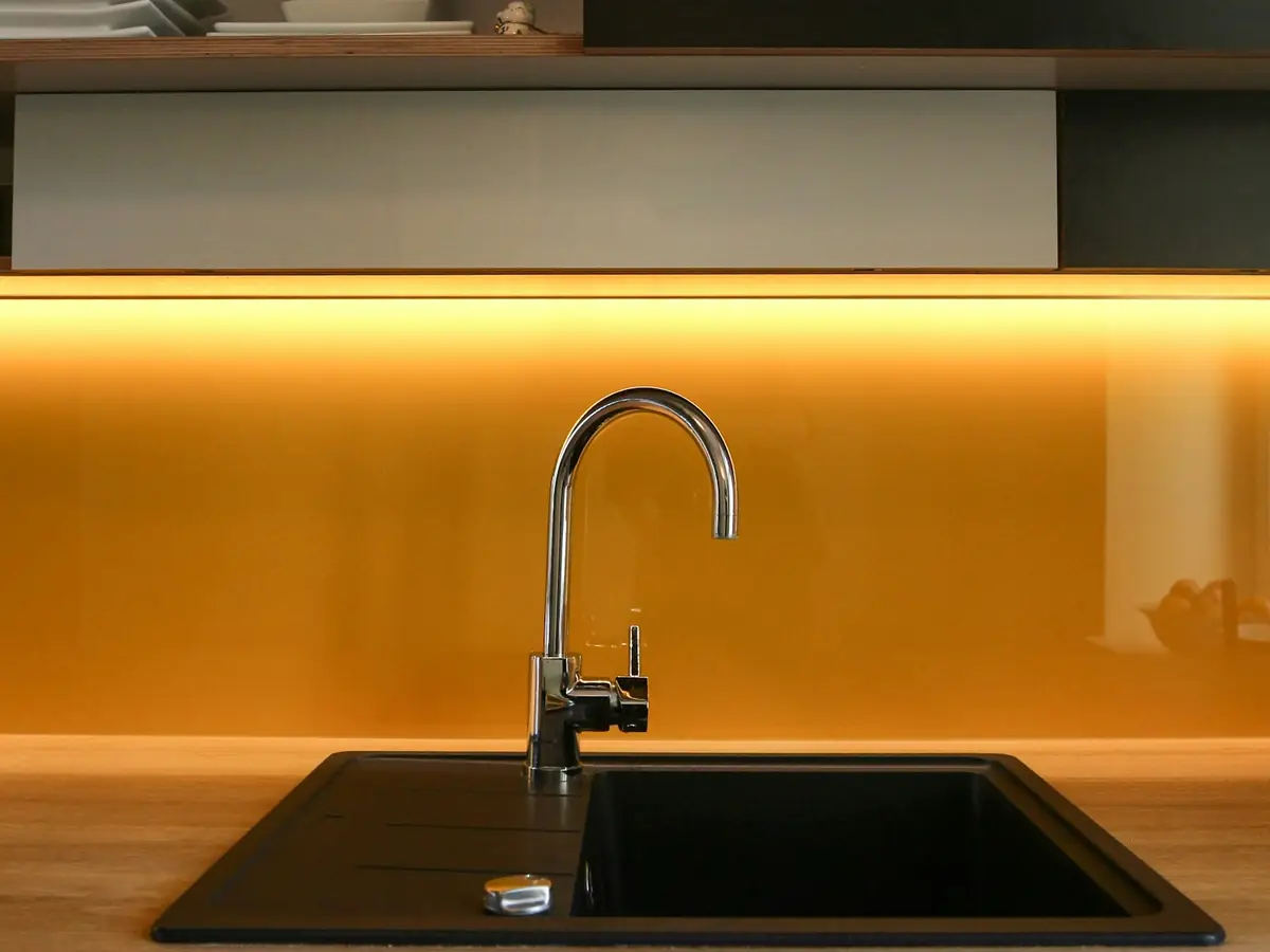 A chrome kitchen faucet over a black sink under cabinet lighting