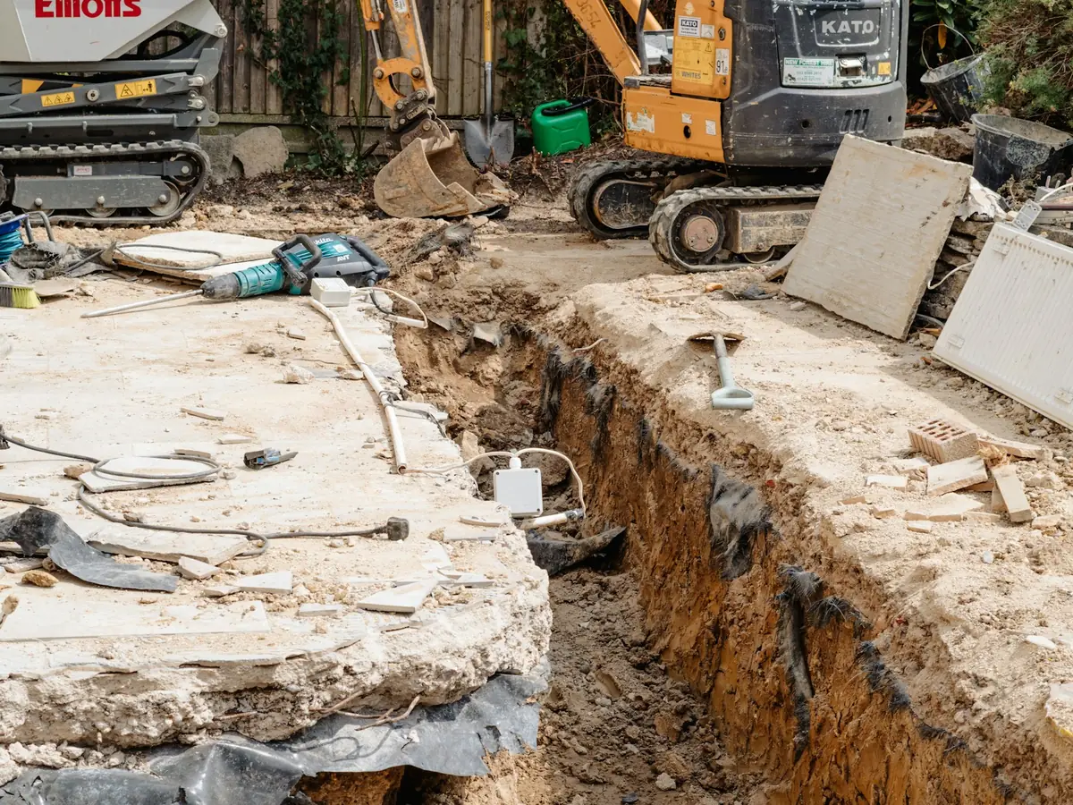 A mini excavator digging a trench in a yard for underground pipe work