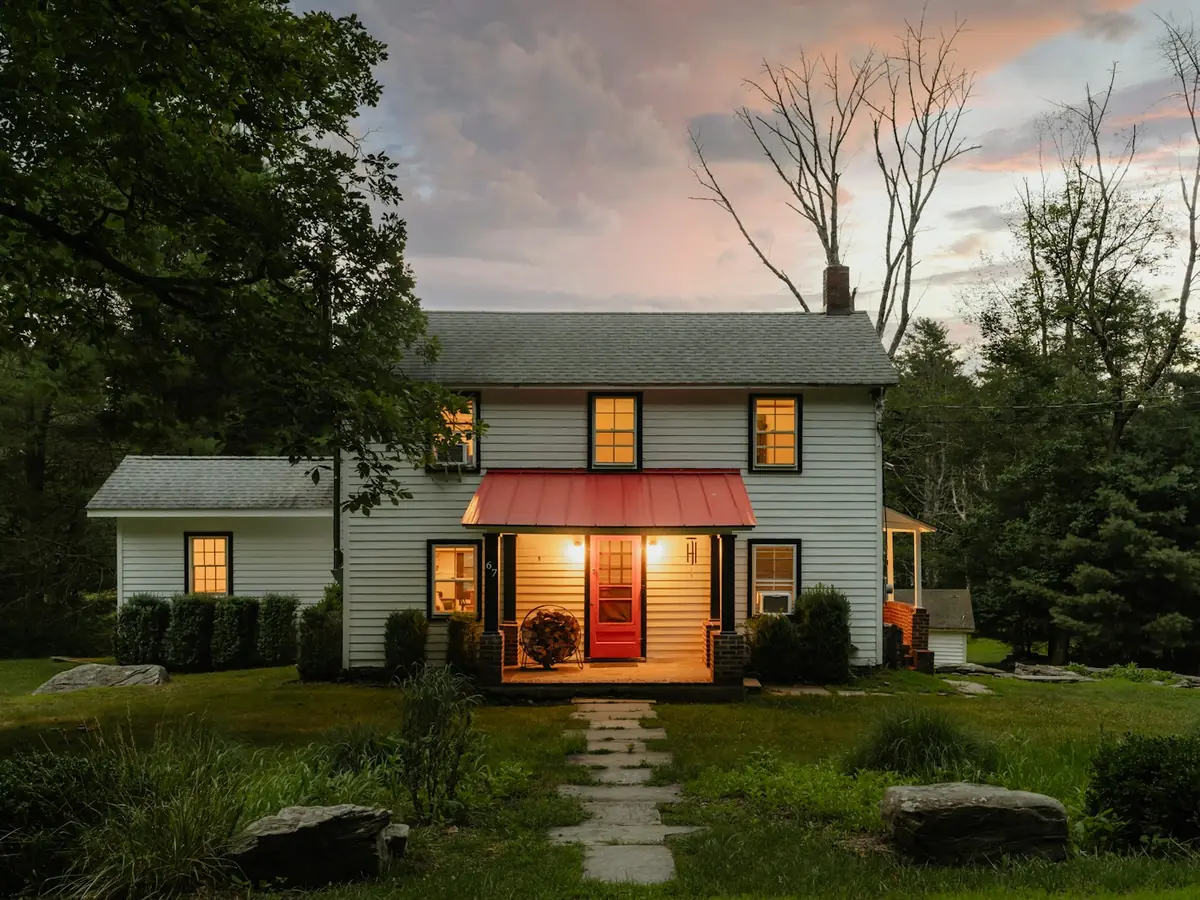 An older two-story house with a lit front porch at dusk
