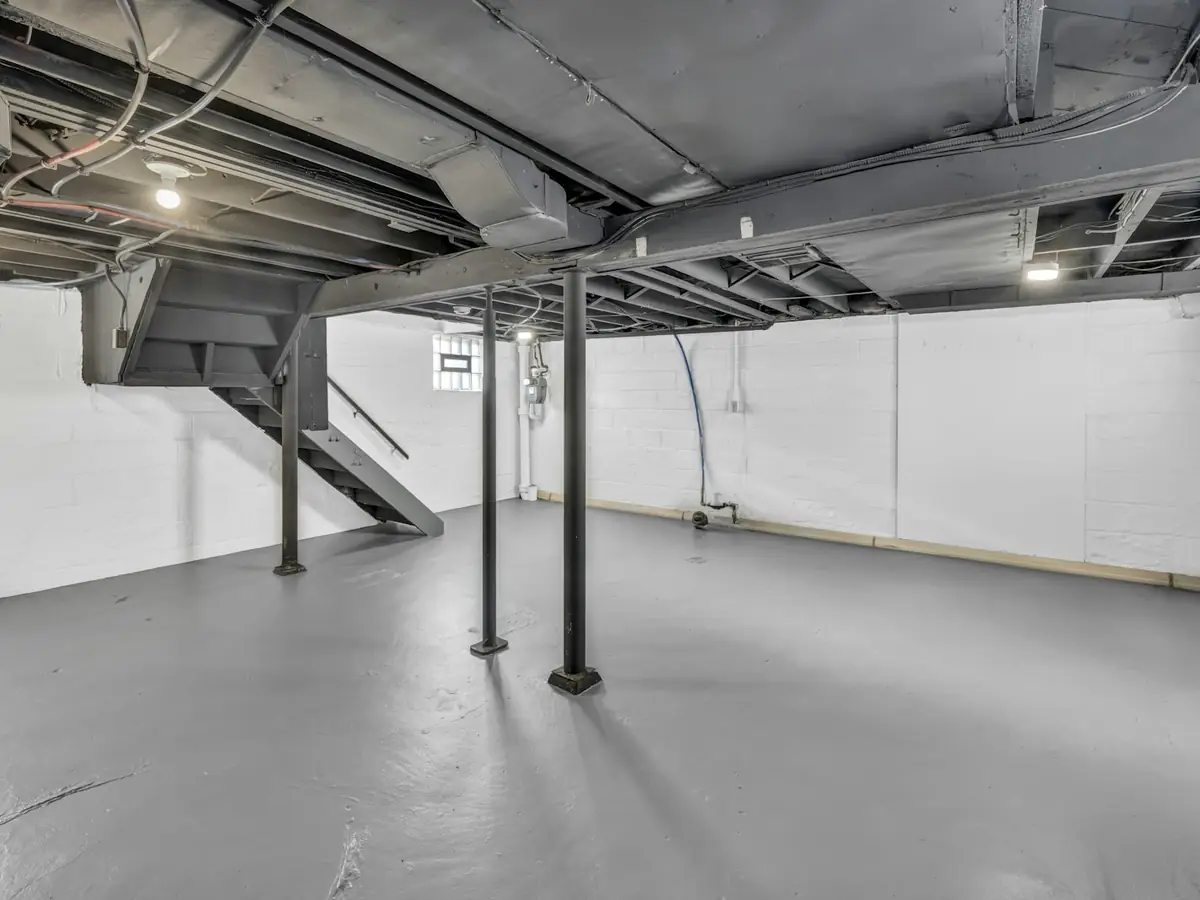 An unfinished basement with a concrete floor and steel support posts