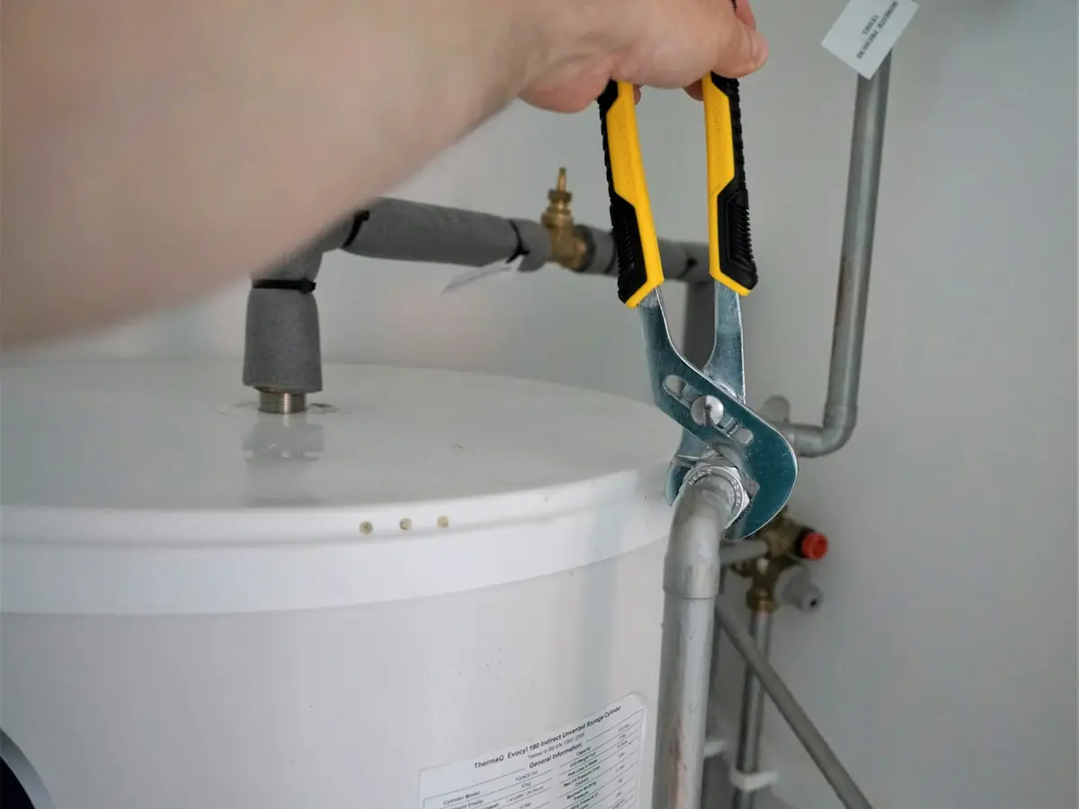 Pliers on a pipe fitting above a white water heater tank